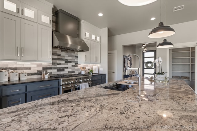 kitchen with pendant lighting, double oven range, white cabinets, wall chimney range hood, and decorative backsplash