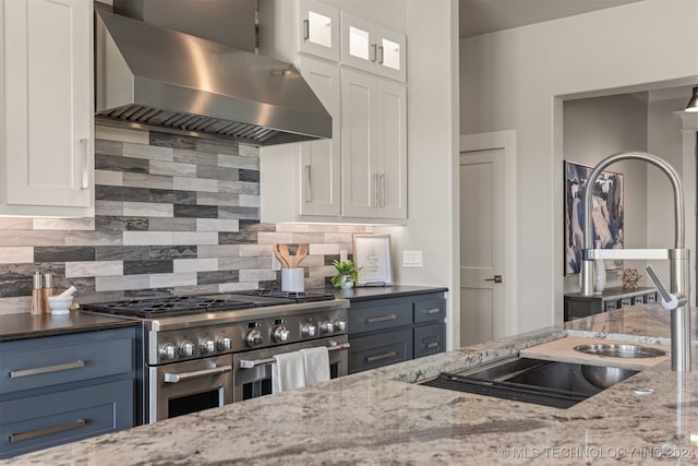 kitchen featuring dark stone counters, white cabinets, double oven range, and wall chimney range hood