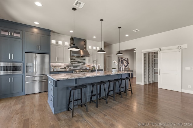 kitchen with stainless steel appliances, pendant lighting, a barn door, a large island with sink, and stone counters