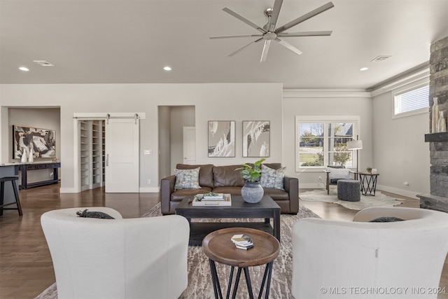 living room featuring ceiling fan, dark wood-type flooring, a barn door, crown molding, and a fireplace