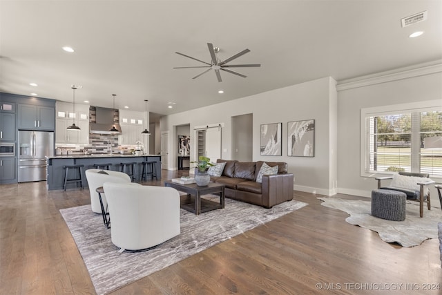 living room featuring a barn door, dark hardwood / wood-style floors, ceiling fan, and ornamental molding