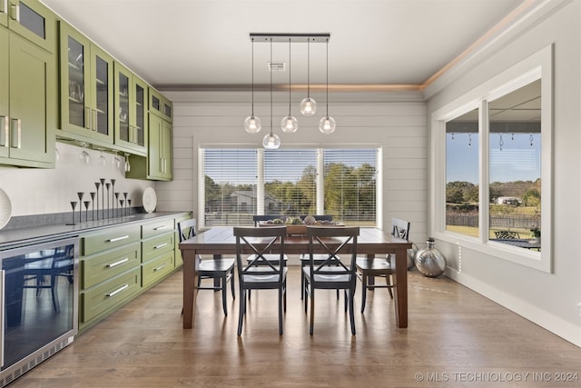 dining space featuring a healthy amount of sunlight, wood-type flooring, crown molding, and wine cooler