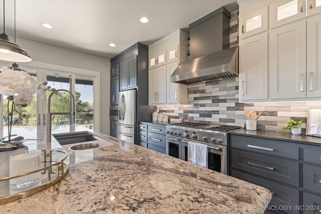 kitchen with sink, wall chimney exhaust hood, stainless steel appliances, pendant lighting, and white cabinets