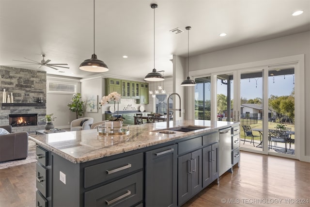 kitchen featuring ceiling fan, a stone fireplace, a kitchen island with sink, and hanging light fixtures