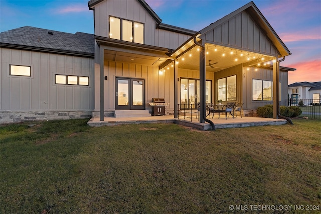 back house at dusk with a lawn, ceiling fan, and a patio area