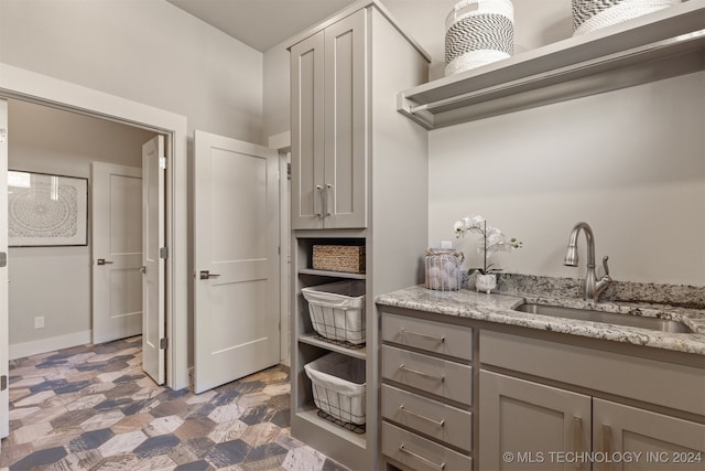 kitchen with light stone countertops, gray cabinetry, and sink