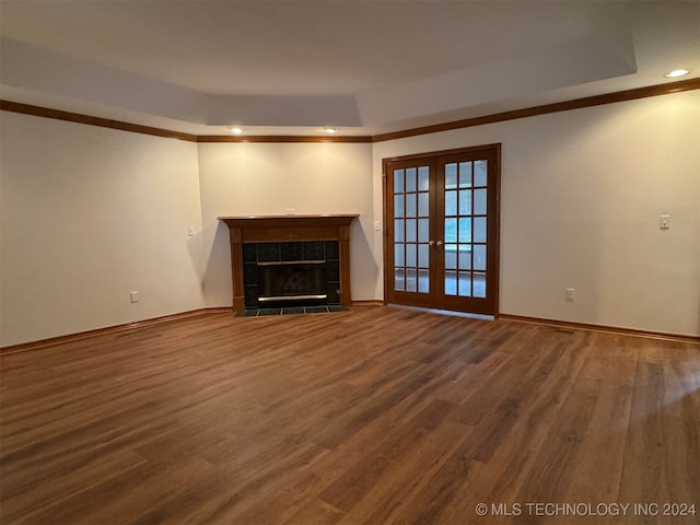 unfurnished living room with a tiled fireplace, wood-type flooring, a raised ceiling, crown molding, and french doors