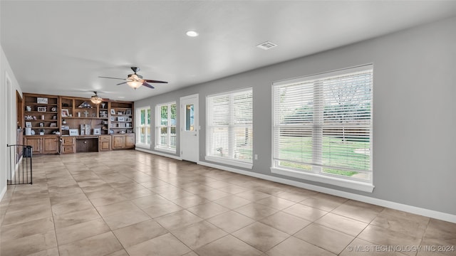 unfurnished living room with light tile patterned floors, built in desk, and a wealth of natural light