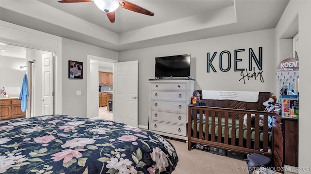 bedroom with light carpet, connected bathroom, a raised ceiling, and ceiling fan