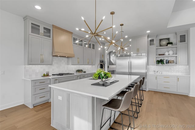 kitchen featuring stainless steel appliances, a large island with sink, light hardwood / wood-style floors, and custom exhaust hood