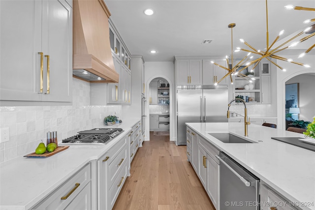 kitchen with stainless steel appliances, light stone countertops, custom exhaust hood, hanging light fixtures, and light wood-type flooring