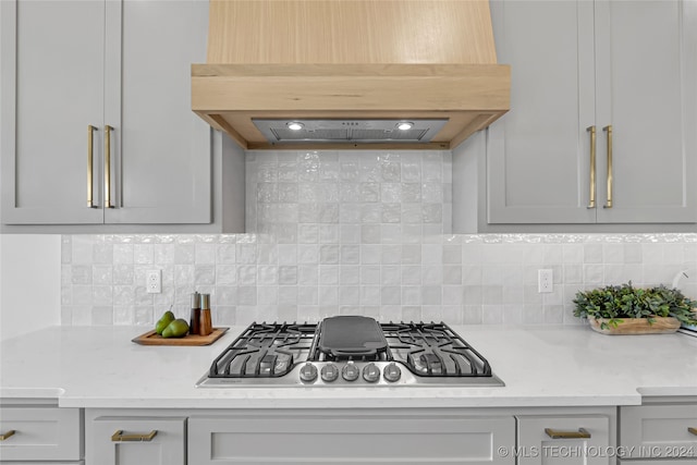 kitchen featuring tasteful backsplash, light stone countertops, stainless steel gas cooktop, and custom range hood