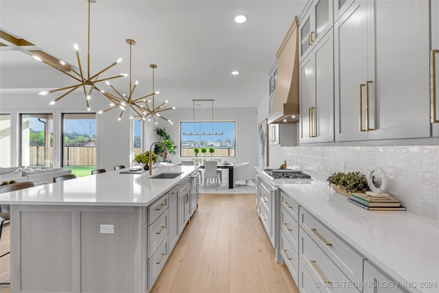 kitchen with backsplash, a large island, decorative light fixtures, sink, and light hardwood / wood-style floors