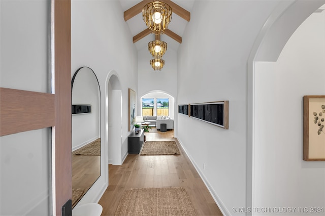 hall with light hardwood / wood-style floors, beamed ceiling, high vaulted ceiling, and a notable chandelier