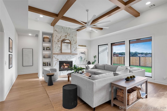 living room featuring light hardwood / wood-style floors, a premium fireplace, coffered ceiling, ceiling fan, and beam ceiling