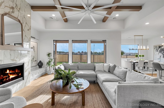 living room featuring beamed ceiling, ceiling fan with notable chandelier, a fireplace, light hardwood / wood-style flooring, and coffered ceiling