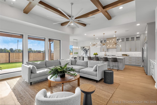 living room featuring light wood-type flooring, ceiling fan with notable chandelier, beamed ceiling, and coffered ceiling