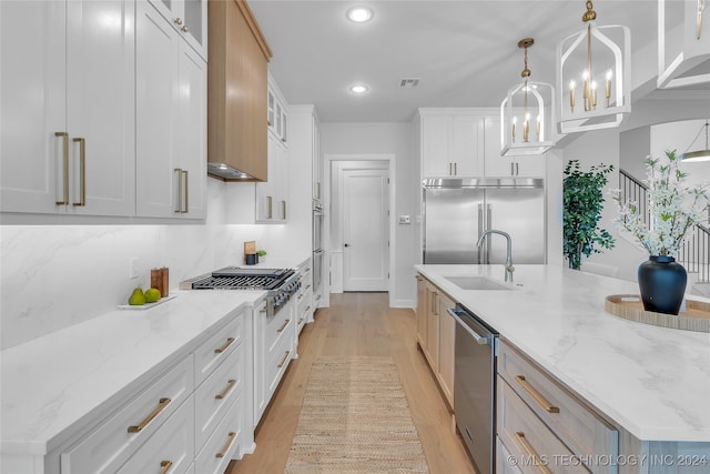 kitchen featuring white cabinets, appliances with stainless steel finishes, pendant lighting, and an island with sink