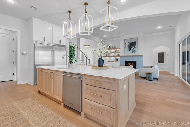 kitchen with sink, light wood-type flooring, decorative light fixtures, and a kitchen island with sink