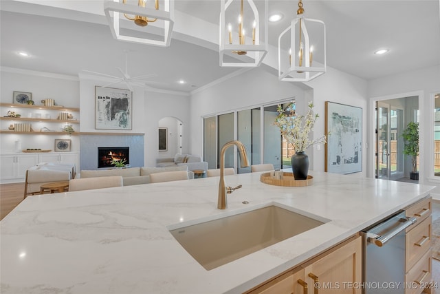 kitchen with ornamental molding, light brown cabinetry, light stone countertops, hanging light fixtures, and sink