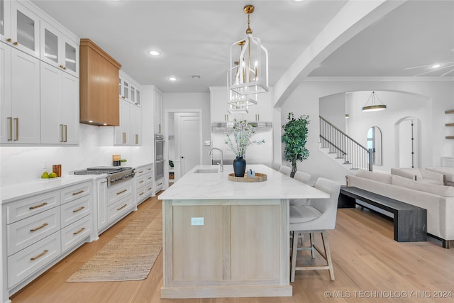 kitchen with white cabinetry, appliances with stainless steel finishes, sink, light hardwood / wood-style floors, and a kitchen island with sink