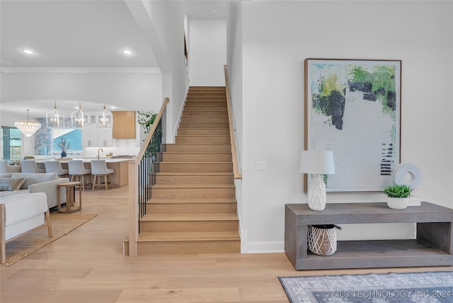 staircase with hardwood / wood-style floors, a notable chandelier, and crown molding