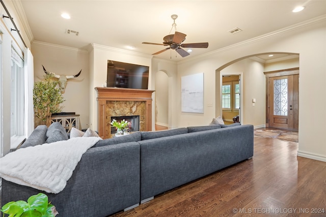 living room featuring dark wood-type flooring, a premium fireplace, ceiling fan, and crown molding