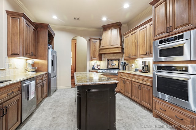 kitchen featuring appliances with stainless steel finishes, custom range hood, backsplash, crown molding, and a center island