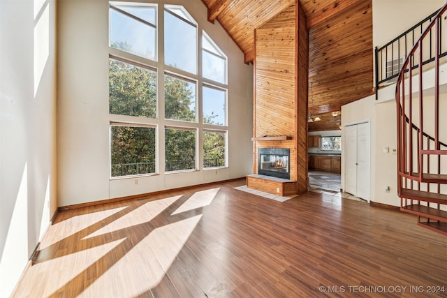 unfurnished living room featuring a stone fireplace, wood-type flooring, wooden ceiling, high vaulted ceiling, and beamed ceiling