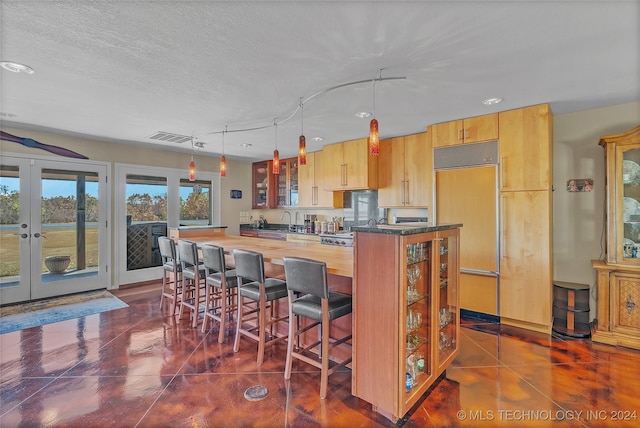 kitchen with french doors, a textured ceiling, paneled refrigerator, pendant lighting, and a breakfast bar