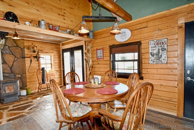 dining area with beamed ceiling, plenty of natural light, wood walls, and a wood stove