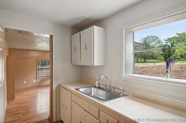 kitchen featuring a healthy amount of sunlight, white cabinetry, sink, and light hardwood / wood-style flooring