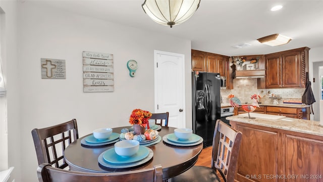 kitchen featuring tasteful backsplash, wood-type flooring, light stone countertops, and black refrigerator with ice dispenser