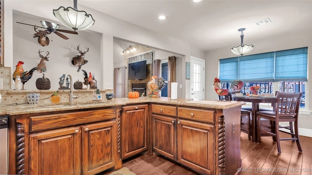 kitchen with pendant lighting, sink, dark wood-type flooring, light stone counters, and kitchen peninsula