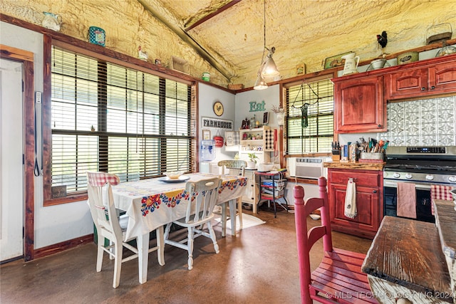 kitchen with a wall unit AC, decorative light fixtures, vaulted ceiling, and stainless steel range oven