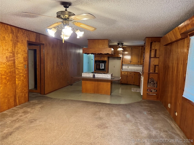 kitchen with kitchen peninsula, a textured ceiling, wooden walls, and stainless steel oven