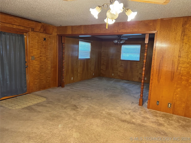 spare room featuring wood walls, carpet, ceiling fan with notable chandelier, and a textured ceiling