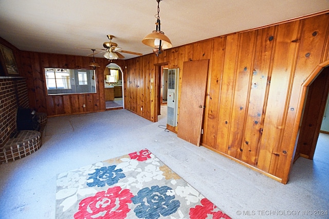 unfurnished living room with a brick fireplace, light colored carpet, wooden walls, and ceiling fan