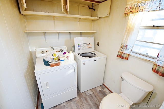 laundry room featuring washing machine and clothes dryer, wood walls, and light hardwood / wood-style flooring