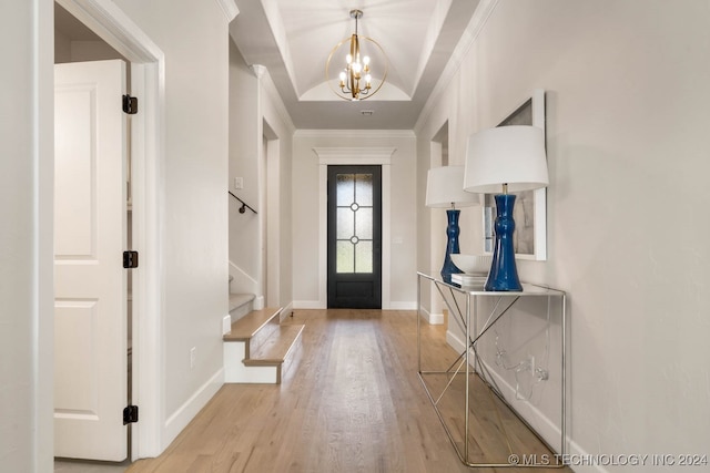 entryway featuring light wood-type flooring, an inviting chandelier, ornamental molding, and a raised ceiling