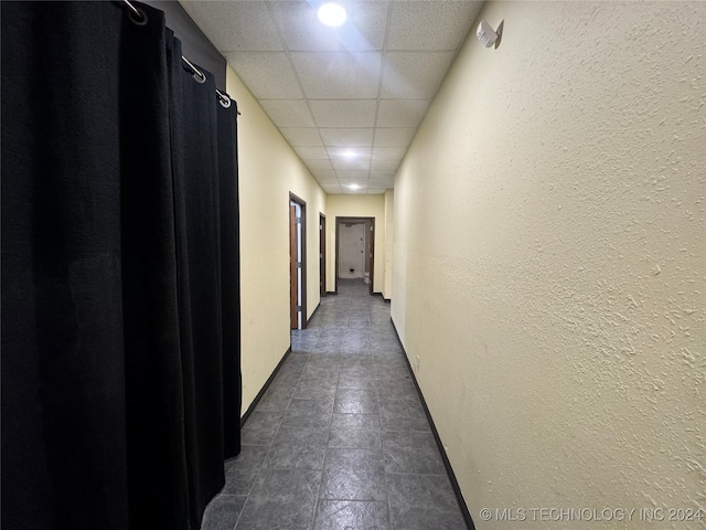 hall featuring dark tile patterned flooring and a paneled ceiling