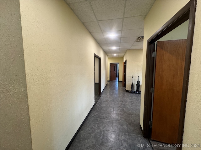 hallway with dark tile patterned floors and a drop ceiling