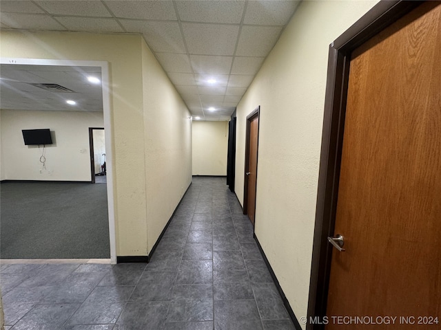 hallway featuring a paneled ceiling and dark colored carpet