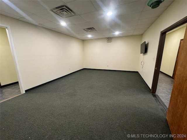 spare room featuring dark carpet and a drop ceiling