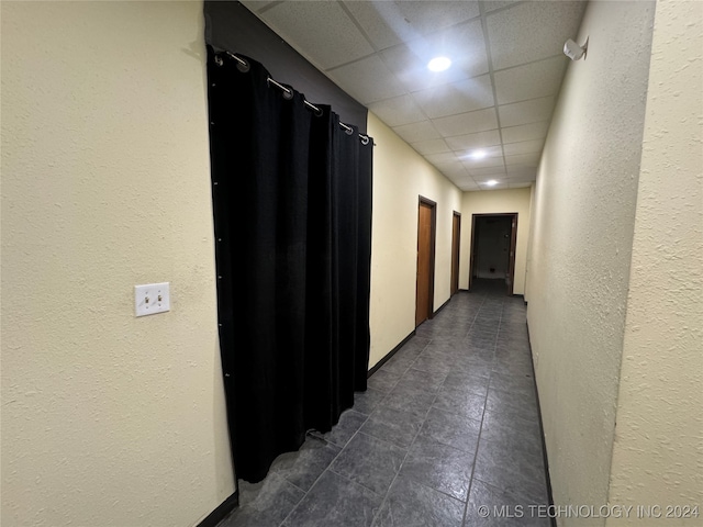 hall with dark tile patterned floors and a paneled ceiling