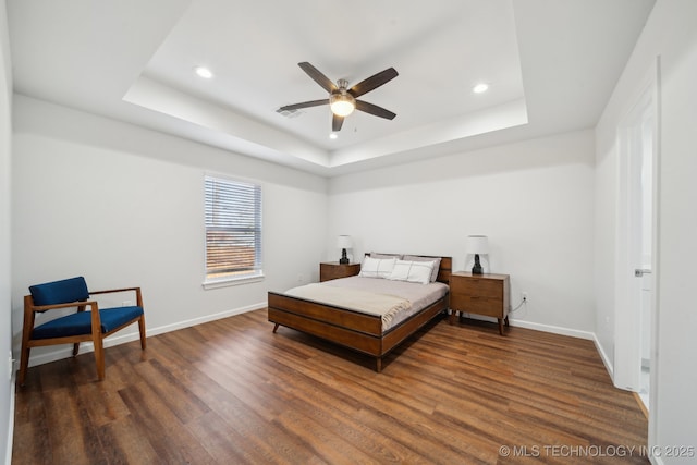 bedroom with dark wood-type flooring, ceiling fan, and a tray ceiling