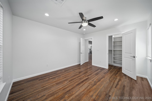 unfurnished bedroom featuring a closet, a walk in closet, dark hardwood / wood-style floors, and ceiling fan