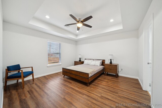 bedroom with ceiling fan, a tray ceiling, and dark hardwood / wood-style flooring