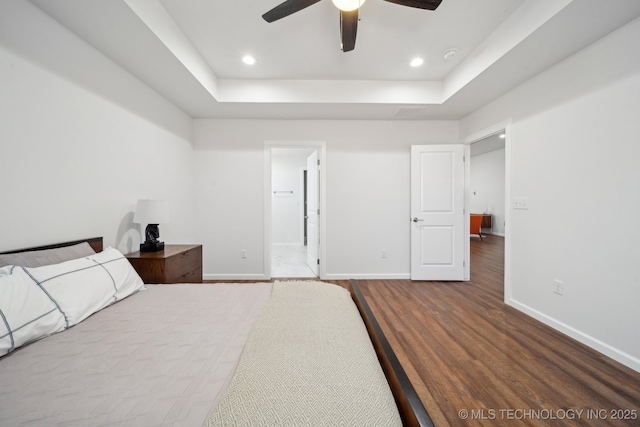 bedroom with dark hardwood / wood-style floors, ceiling fan, and a tray ceiling