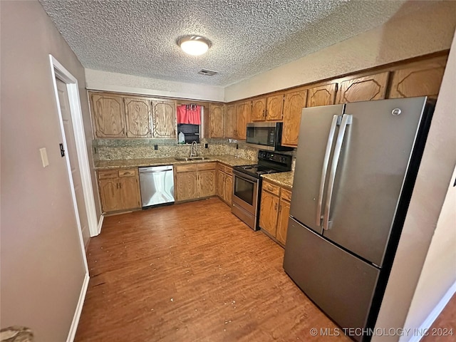 kitchen featuring appliances with stainless steel finishes, sink, backsplash, a textured ceiling, and light hardwood / wood-style flooring